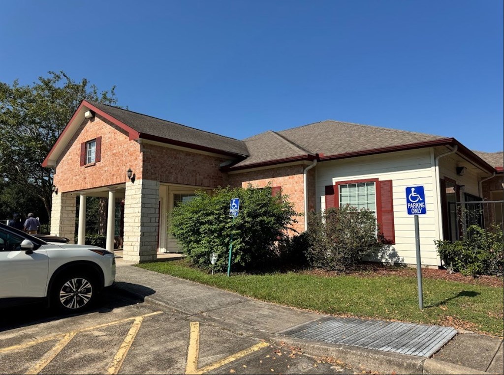 A parking lot with a car parked in front of a building with a handicap sign.