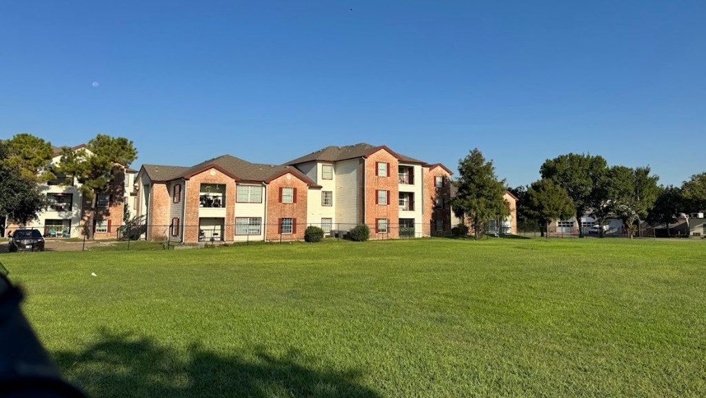 A large grassy field in front of a multi-story apartment building.