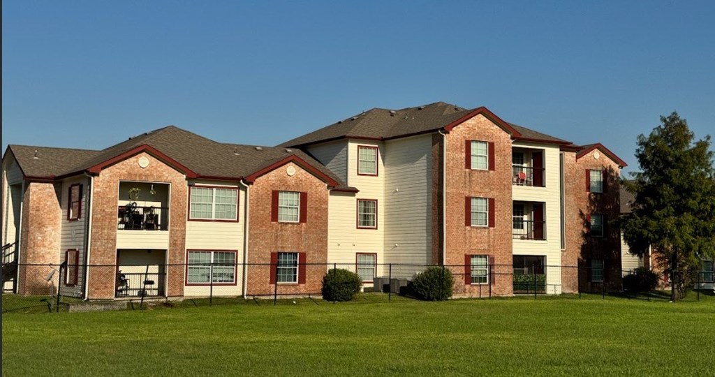 A large brick apartment building with a green lawn in front.