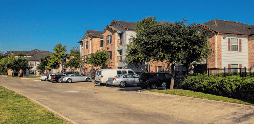 A residential street with houses on both sides and cars parked along the curb.