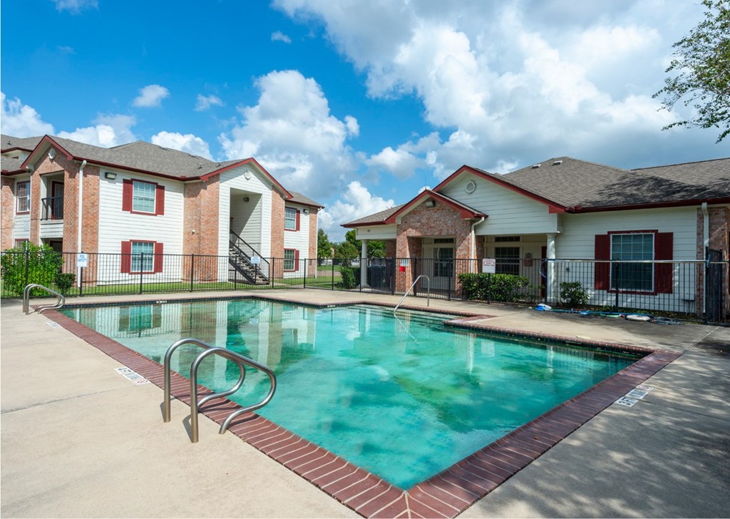 A swimming pool surrounded by a red brick border in front of apartment buildings.