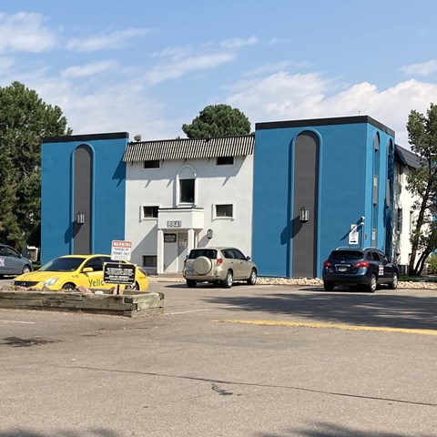 A yellow car is parked in front of a white and blue building.