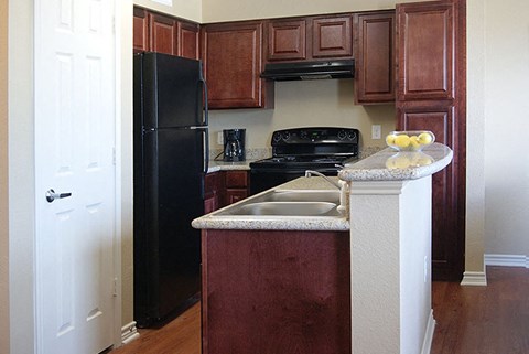 A kitchen with a black refrigerator and brown cabinets.