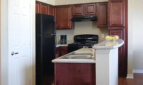 A kitchen with a black refrigerator and brown cabinets.