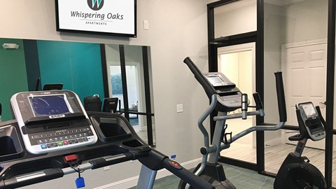 A Whispering Oaks Apartments gym with a treadmill and elliptical trainer.