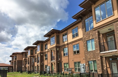A row of brown brick apartment buildings with green shutters and balconies.