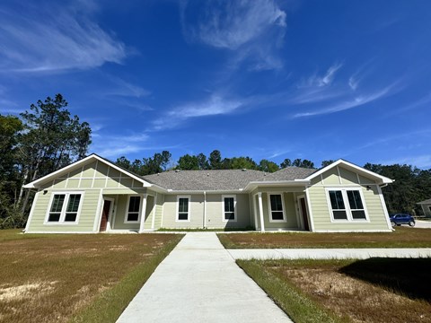 A house with a grey roof and white walls is surrounded by a grassy area.