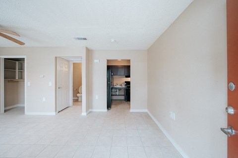 an empty living room with a kitchen in the background