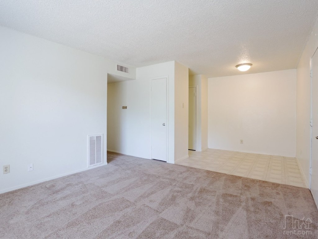 the living room and dining room of an apartment with white walls and flooring