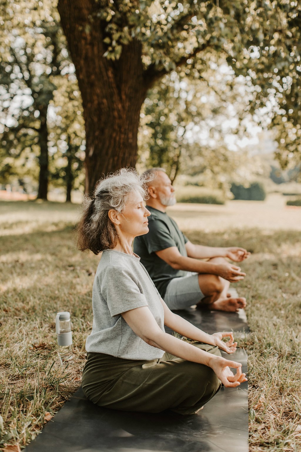 a man and a woman sitting on a yoga mat in a park