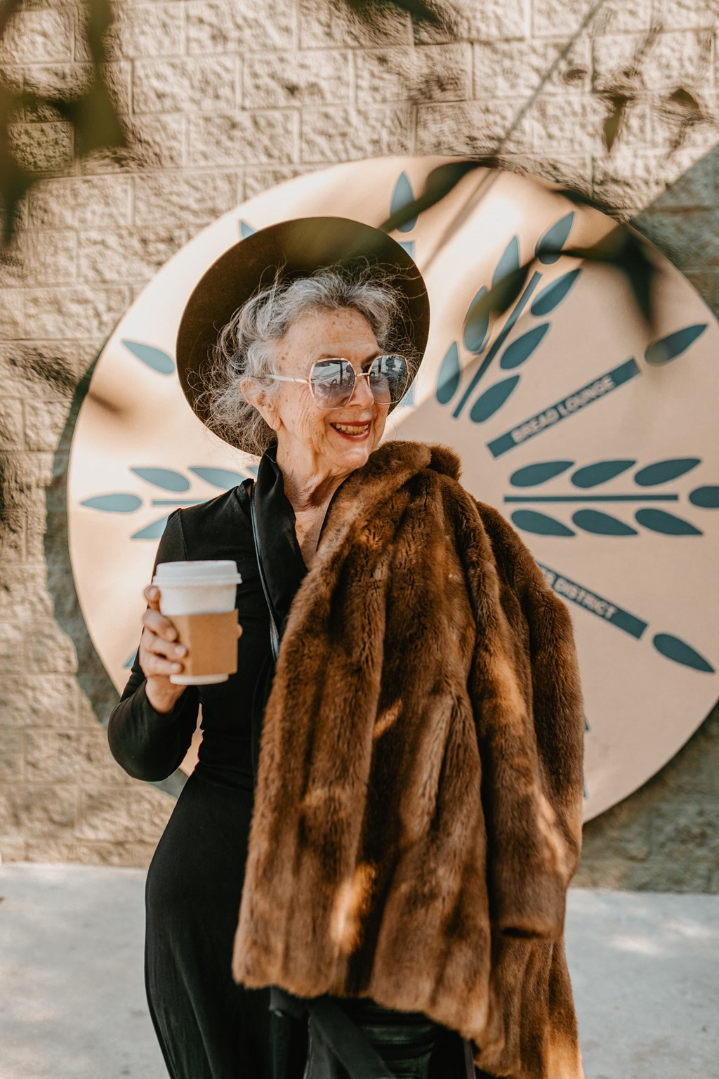 an older woman wearing a hat and a fur coat holding a cup of coffee