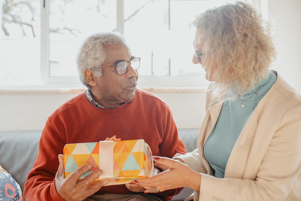 an older couple sitting on a couch holding a christmas present