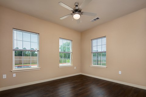 an empty living room with a ceiling fan and three windows