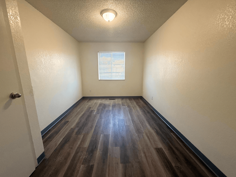 A room with wooden flooring and a window with blinds at Willow Grove Apartments, Clifton, Colorado.