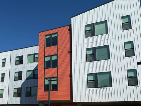 A red building stands out next to white buildings with black windows.
