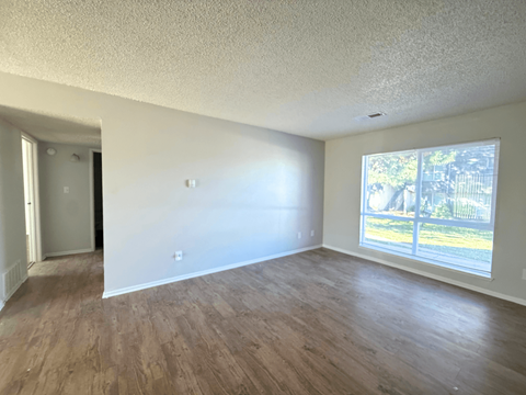 A room with wooden floors and a window showing a view of a fence and trees at Mountain Terrace Apartments, Westminster, Colorado