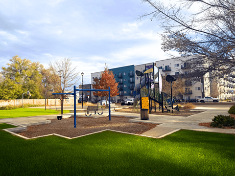 A park with a playground and a building in the background.
