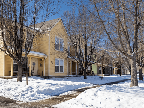 A yellow house with snow on the ground and bare trees at Meeker Commons Apartments, Greeley