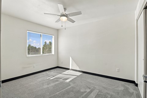 A room with a ceiling fan and a window showing a view of trees at Gateway Village Apartments in Fort Morgan, CO, 80701