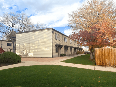 A building with a grey facade is surrounded by a green lawn and a wooden fence.