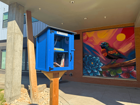 A blue mailbox is on a wooden post outside a building.