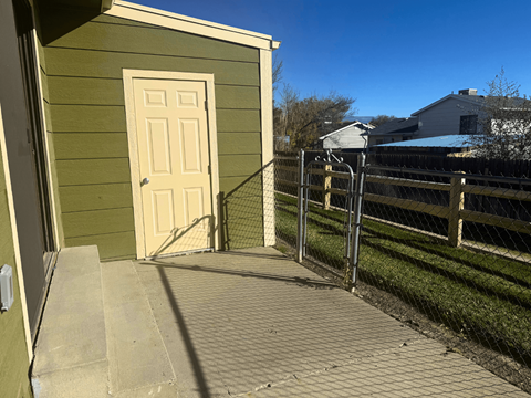 A small green building with a white door and a metal fence.