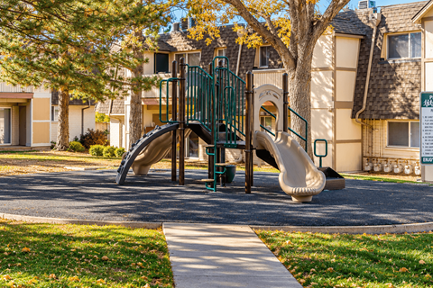 A playground with a slide and a green fence.