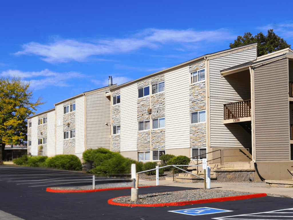 A parking lot in front of a building with a blue handicap parking sign.