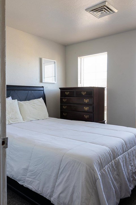A bedroom with a bed, dresser, and window.