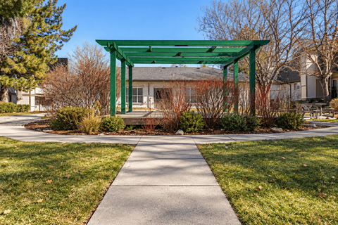 A green pergola is situated in the middle of a grassy area with a concrete walkway leading to it.