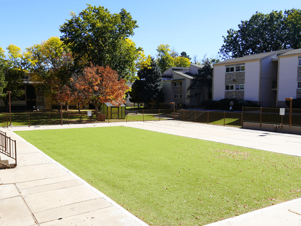 A grassy area in front of a building with trees in the background.