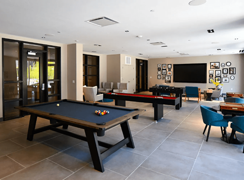 A pool table is in the middle of a room with a bar and a TV.