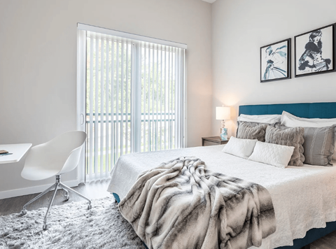 A bedroom with a large bed, a chair, and a window with blinds.