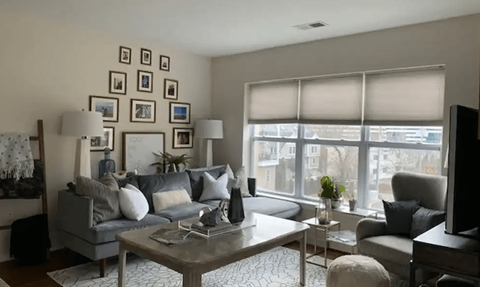 A living room with a grey couch, a coffee table, and a large window with blinds.