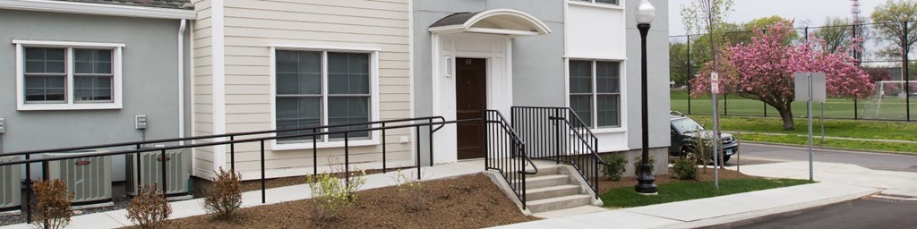 A grey house with a black railing and a brown door.