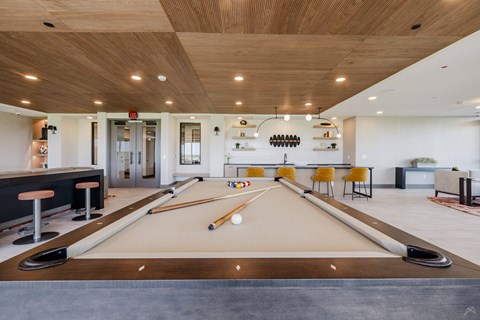 A pool table is in the middle of a room with a bar and a kitchen in the background.