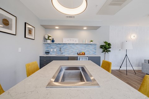 A modern kitchen with a marble table and yellow chairs.