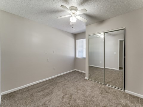 an empty bedroom with a mirrored closet and a ceiling fan