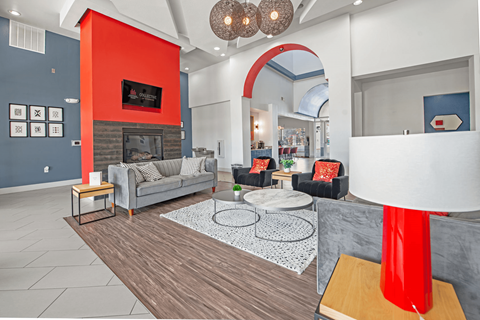 A living room with a grey couch and a red accent wall.