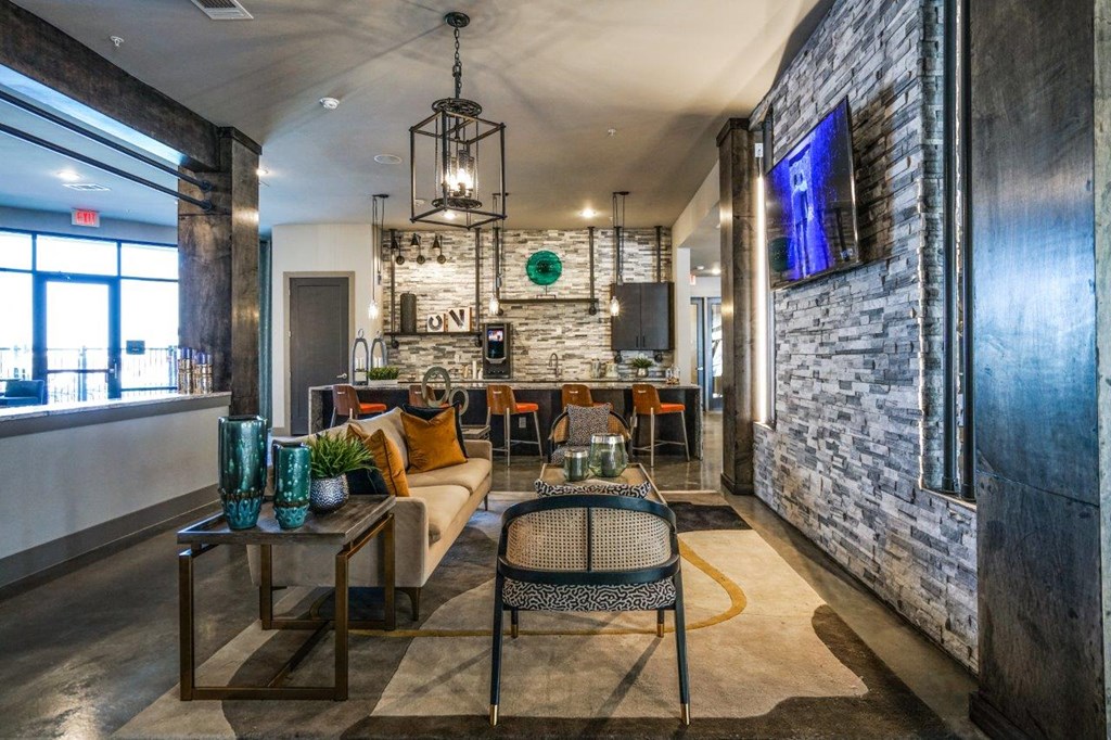 A modern living room with a stone wall and a flat screen TV at The Grand at Manor Apartments, Manor, Texas