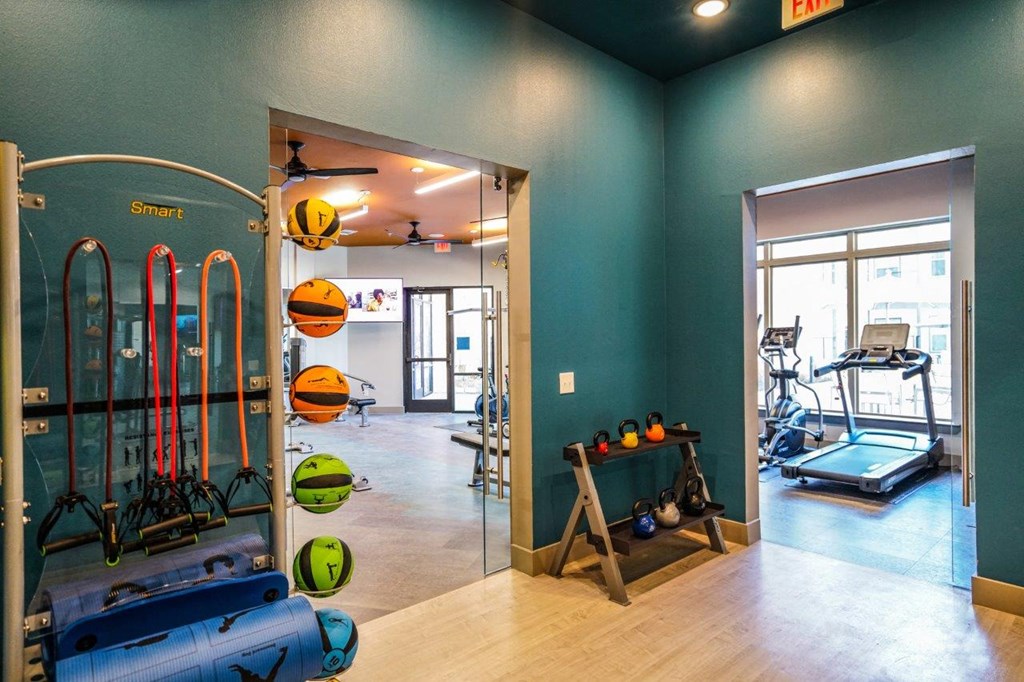 A gym with a row of exercise equipment including a treadmill, a rowing machine, and a stationary bike at The Grand at Manor Apartments, Texas