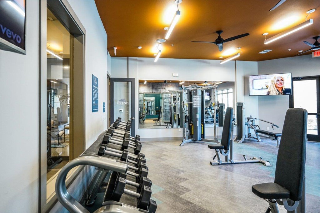 A gym with a row of treadmills on the left and a variety of other equipment in the background at The Grand at Manor Apartments, Manor, TX, 78653