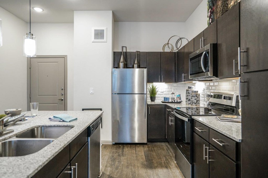 A modern kitchen with a stainless steel refrigerator and black cabinets at The Grand at Manor Apartments, Manor, TX