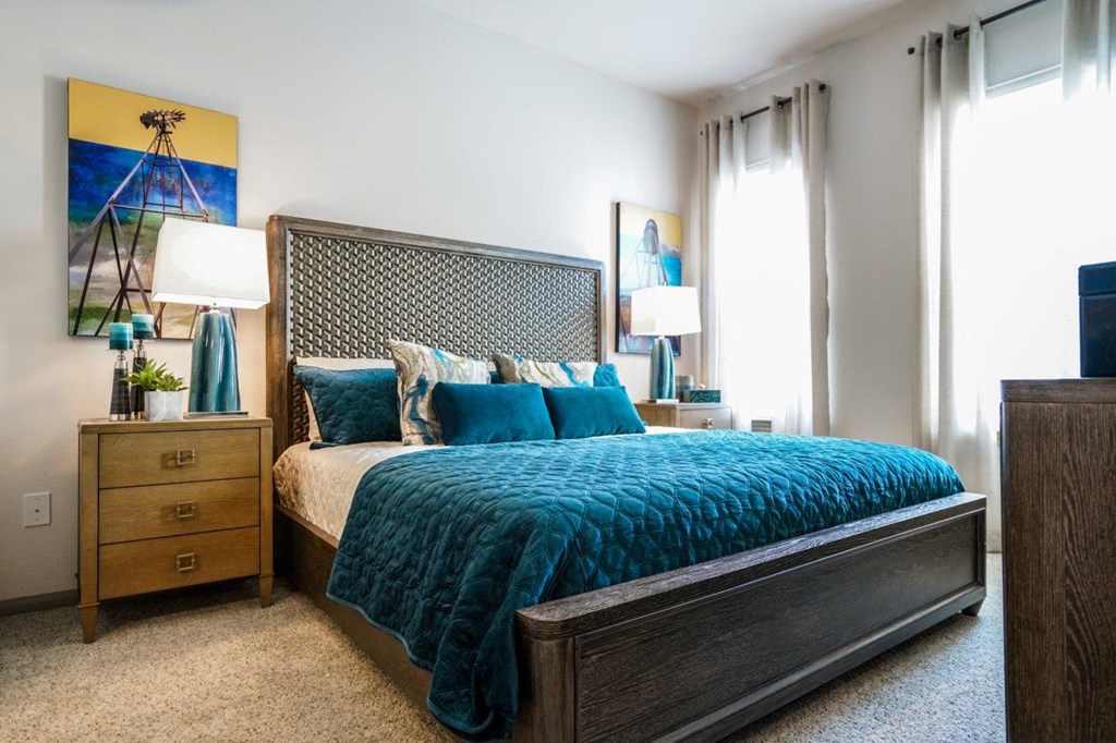 A bedroom with a bed, nightstand, and a painting on the wall at The Grand at Manor Apartments, Manor, 78653