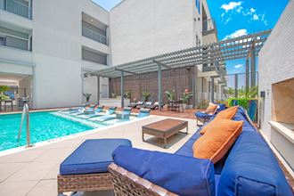 a patio with blue couches and orange pillows and a pool in the background