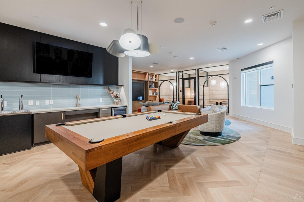 A pool table is in the middle of a room with a TV and a bar.