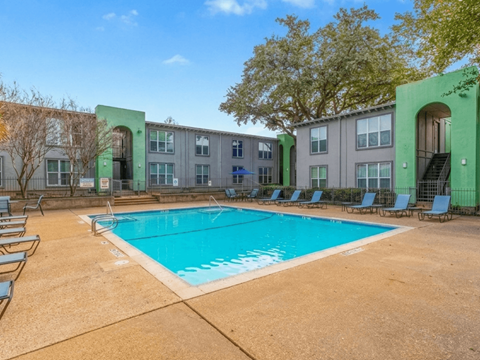 A swimming pool surrounded by chairs and trees in front of a building.