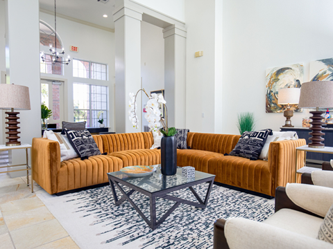 A living room with a large orange couch and a glass coffee table.