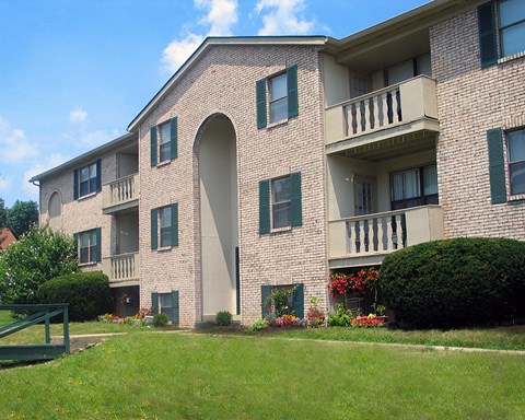 a large brick apartment building with a green lawn and bushes  at Four Worlds Apartments, Cincinnati