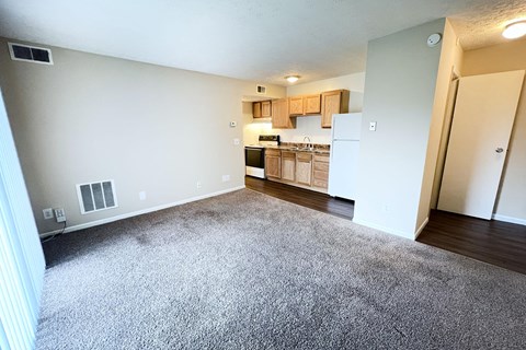 A room with a carpeted floor and a kitchen area in the background at Crown Crossing Apartments, Amelia, Ohio 45102